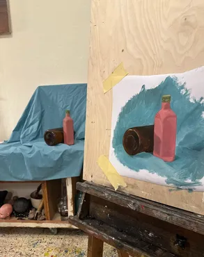 Still life painting of bottles on blue fabric, on an easel
